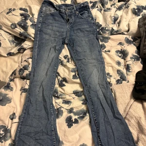 Blå bootcut jeans med detaljerade fickor - Snygga blå jeans med bootcut-modell och coola bakfickor med vita sömmar och knappar. Jeansen har klassisk femficksdesign och är tillverkade i ett mjukt denimtyg. Perfekta för dig som gillar en retroinspirerad look med lite extra detaljer. Petite modell