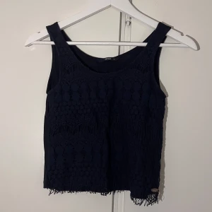 Mörkblå spetslinne från ONLY - Snyggt mörkblått linne från ONLY i storlek XS. Toppen har ett spetslager med mönster, och fransar längst ner.