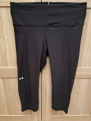 Svarta kompressionstights Under Armour - Svarta kompressionstights från Under Armour med hög midja och diskret logga på benet. Tillverkade i stretchigt syntetmaterial som sitter tight och ger stöd vid träning. Använda och tvättade 1 gång. 
