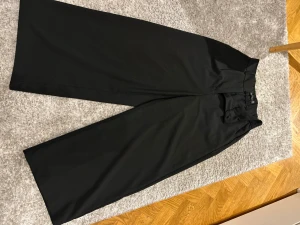 Svarta wide kostymbyxor från Amisu - Säljer ett par svarta kostymbyxor från Amisu i storlek 32. Byxorna har hög midja, breda ben och klassisk kostymlook. Materialet är mjukt och har en snygg struktur, perfekt för dig som gillar en stilren och modern vibe.