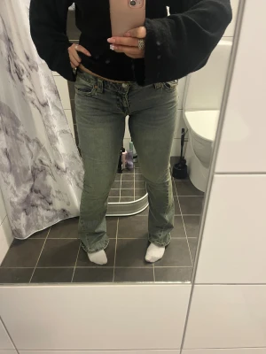True Religion blå bootcut jeans - Säljer ett par blå jeans från True Religion med bootcut och klassiska fickdetaljer med knapp bak. Jeansen har låg midja och är tillverkade i jeansmaterial med snygga slitningar och kontrastsömmar.