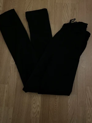 Svarta mjukisbyxor med snörning - Svarta mjukisbyxor med resår och snörning i midjan. Byxorna är i mjukt material och har en klassisk loose passform, perfekta för chill eller träning. Insidan är fleecefodrad för extra komfort.