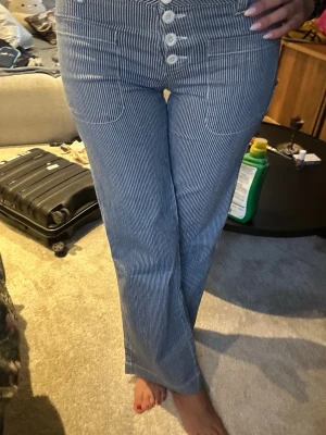 Randiga vintage blå byxor  - Jätte fina blå randiga trendiga low waist jeans. Jeans material men de är lite stretchiga i materialet så de formar sig efter bena på ett snyggt sätt. Tyvärr är de för små för mig som är 177 och har M/L i byxor så de sitter lite tight på mig. Vintage stil. Skulle säga att de passar storlek S/M i och med att de har stretchiga material.