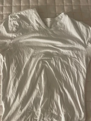 Vit kortärmad t-shirt från BOSS - Säljer en vit t-shirt från BOSS med broderad logga på bröstet. T-shirten har en klassisk v-ringad hals och är tillverkad i mjuk bomull. Perfekt för dig som gillar stilrena och enkla plagg med diskret branding.