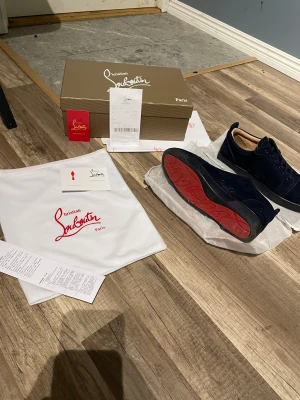Mörkblå sneakers från Christian Louboutin - Säljer ett par mörkblå sneakers från Christian Louboutin med klassisk röd sula och snygg snörning. Skorna är tillverkade i mocka och har en rund tå samt platt sula. Medföljer originalkartong, dustbag och äkthetskort. Skorna är helt nya och jag har använt dom typ  4 gånger, jag köpte dom för 2000 men jag säljer dom för 1800.     Skriv vid funderingar 