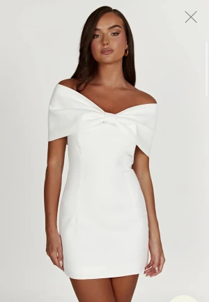 Vit miniklänning med rosett - Vit off-shoulder klänning med figurnära passform och rosettdetalj framtill. Perfekt till student, fest eller bröllop.                                                         Endast provad!                                                    Säljes då den var för liten och ej går att returnera. Nypris 1700kr. (pris går att diskutera🫶🏻)