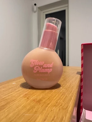 Glow and Plump Glass Skin Drops - Glow and Plump Glass Skin Drops från Glowid i en rund, ljusrosa flaska med pump och genomskinligt lock. Perfekt för att ge huden extra lyster och en plumpad känsla. Snygg design med rosa text på flaskan. Se mängd på bilden. 