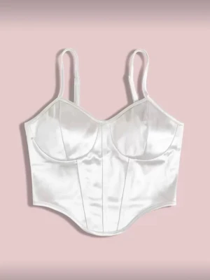 Vit satin korsett med smala axelband - Snygg vit korsett i satin med smala justerbara axelband och markerade kupor. Toppen har en figurnära passform och stilrena sömmar framtill som ger en cool siluett. Perfekt att styla med jeans eller kjol för en trendig look. Aldrig använd. 