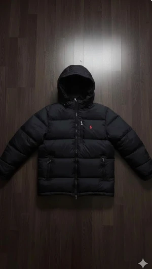 Svart pufferjacka Polo Ralph Lauren M - Svart pufferjacka från Polo Ralph Lauren i storlek M. Jackan har huva, dragkedja framtill och två sidofickor med dragkedja. Klassisk design med röd Polo-logga på bröstet. Perfekt för kalla dagar och har en schysst, lite oversized look.