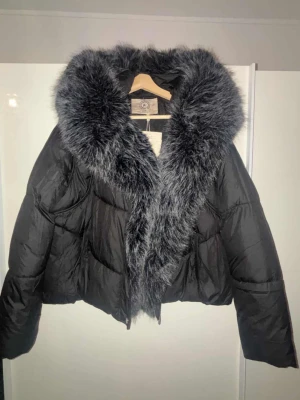 Svart pufferjacka med päls - Säljer en svart pufferjacka från Rock and Blue med stor fluffig konstpäls i grått runt kragen. Jackan är croppad och har en riktigt snygg oversized look. Perfekt för kalla dagar när du vill vara både varm och stilren. Inte Använd någon gång
