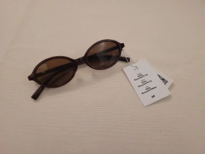 Ovala solglasögon från H&M - Snygga solglasögon med oval form och rödbruna bågar i återvunnen plast. Glasen är tonade i brunt och skalmarna har guldfärgade detaljer längst ut. Perfekt accessoar för att höja din stil och skydda ögonen mot solen.