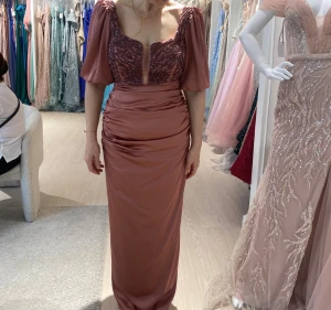 Rosa långklänning med paljetter - Säljer en elegant långklänning i rosa med glittrig paljettdekor på livet och puffiga kortärmar. Klänningen har en djup v-ringning och är tillverkad i ett satinliknande material med rynkade detaljer vid midjan. Perfekt för speciella tillfällen!