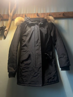 Svart parkajacka med äkta päls från The Love Band - Parkajacka i svart med fluffig äkta päls runt huvan, perfekt för kalla dagar. Jackan har långa ärmar, två snedställda fickor och stängs med dragkedja och knappar. Materialet är nylon och polyester. Storlek M 💕🥰 obs! Pälsen går att ta bort.  Jätte fint skick, det är bara tvättlappen som trådar. 😊