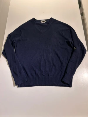 Marinblå kashmirtröja från Peter Millar - Snygg marinblå tröja från Peter Millar i 100% kashmir. V-ringad modell med ribbade muddar vid ärmslut och nederkant. Perfekt för dig som gillar klassisk stil och mjuka material. Långärmad och passar dig som vill ha en lite lyxigare känsla.