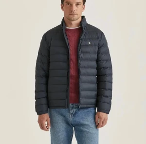 Mörkblå pufferjacka från Morris - Säljer en stilren mörkblå pufferjacka från Morris med diskret logga på bröstet. Jackan har dragkedja framtill, hög krage och quiltad design. Perfekt för kyliga dagar och enkel att matcha med jeans eller chinos. Skulle rekommendera som en höstjacka snarare än en vinterjacka. 