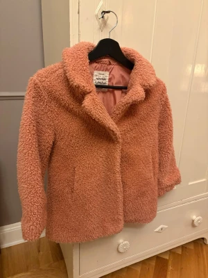 Rosa teddyjacka från Zara strl 128 - Mysig teddyjacka i en snygg rosa färg från Adventure Collection. Jackan har en klassisk krage, långärmade ärmar och är tillverkad i fluffigt teddy-material som ger en cool och trendig look. Perfekt för dig som vill ha en varm och stilren jacka.