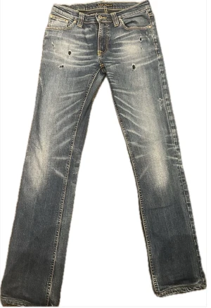 Blå Nudie Jeans W28 L32  - Säljer ett par blå Nudie Jeans med slitna detaljer framtill. Jeansen har klassiska fem fickor, kontrastsömmar och Nudie-logga på bakfickan. Materialet är jeans med en tvättad look och ljusa partier. Perfekt för dig som gillar en avslappnad stil.