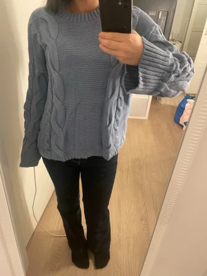 Ljusblå stickad tröja från 157 - Säljer en ljusblå stickad tröja från 157 i storlek XS. Tröjan har grova kabelstickade detaljer längs ärmar och framstycke, samt ribbade muddar vid hals, ärmslut och nederkant. Perfekt för kyliga dagar och har en loose passform med långa ärmar.