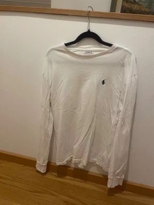 Vit långärmad tröja från Polo Ralph Lauren - Vit långärmad tröja från Polo Ralph Lauren i klassisk fit. Tröjan har rund hals och den ikoniska broderade loggan på bröstet. Tillverkad i mjuk bomull som är skön mot huden. Perfekt för dig som gillar stilrena och enkla plagg.