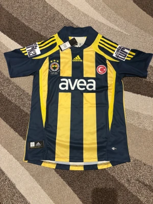 Fenerbahce Retro 07-08 Hemmatröja - Denna Fenerbahce Retro 07-08 Hemmatröja är helt ny och aldrig använd. Den är i Storlek S och är perfekt passform. Den har Alex 10 på ryggen för den brasilianska spelaren Alexsandro de Souza. Den har även sponsorn för den tiden COLA TURKA på sidorna. Skit snygg tröja och skön att ha. Vid frågor är det bara att skriva.