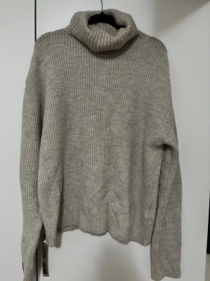 Beige stickad polotröja - Säljer en beige stickad polotröja med grov ribbad krage och långa ärmar. Tröjan har en loose passform och är perfekt för kyliga dagar. Materialet är mjukt och värmande, och den neutrala färgen gör den enkel att matcha med olika outfits.