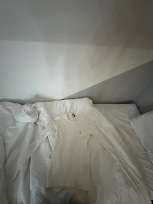 Vit kabelstickad tröja Polo Ralph Lauren - Säljer en vit kabelstickad tröja från Polo Ralph Lauren i storlek S. Tröjan har lång ärm, rund hals och ett rosa broderat Polo-logo på bröstet. Tillverkad i 100% bomull, perfekt för dig som gillar klassisk och stilren design.