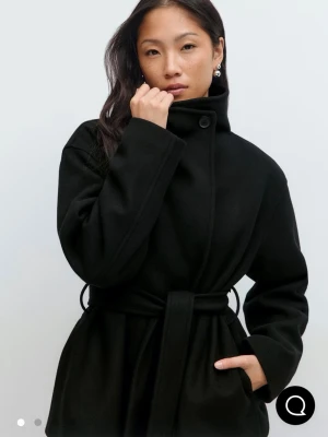 Svart kappa med bälte gina - Köpte denna korta kappan från Gina för 700kr. Hqr haft på mig den max 5 gånger. Som ny. Säljs pågrund av flytt rensning. Jackan heter ”high neck short jacket” på Gina 