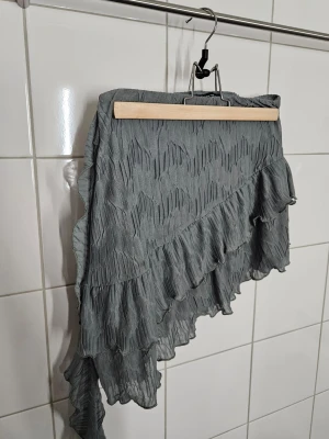 Kort kjol - Asymmetrisk kort kjol med dekorativ kant och hängande detalj ✨️ stretchig i tyget och typ grå/grön i färgen.