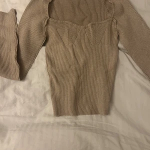 Beige ribbad stickad tröja - Snygg beige stickad tröja med ribbad struktur och unika detaljer vid bröstet. Tröjan har långärmade och en figurnära passform som sitter riktigt bra. 