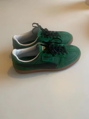 Gröna Puma Super Team sneakers - Säljer ett par gröna Puma Super Team sneakers med svart logga och detaljer. Ovandelen är i mocka och mesh, med svarta skosnören och vit insida. Sulan är i gummi och har ett klassiskt mönster. Perfekta för dig som gillar retrostil och streetwear.
