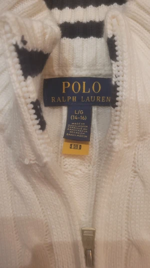 Vit stickad tröja Polo Ralph Lauren - Säljer en vit stickad tröja från Polo Ralph Lauren med klassiskt kabelmönster och halv dragkedja vid halsen. Tröjan har ribbade muddar och en broderad logga på bröstet. Perfekt för dig som gillar stilrena och tidlösa plagg. Nypris 1600, tröjan är aldrig använd. 