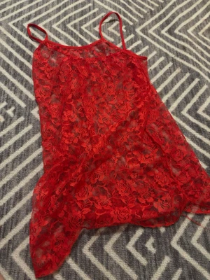 Röd spetsig linnetopp med blommönster - Säljer en röd, transparent linnetopp med tunna axelband och blommigt spetsmönster. Toppen har en lätt och luftig känsla. Märke eller storlek står ej på linnet. Men skulle säga att det är en M/L. Men är väldigt enkel att sy in.