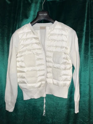Vit cardigan jacka från Moncler - Snygg vit cardigan jacka från Moncler med quiltad front och två fickor. Jackan har långärmade stickade ärmar och ribbad nederkant. Dragkedja framtill och snörning nedtill. Moncler-logga på ärmen. Perfekt för dig som gillar exklusiva märken. Priset är förhandlingsbart❤️