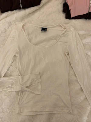 Vit långärmad topp från Gina Tricot - Säljer en enkel och stilren vit långärmad topp från Gina Tricot i storlek XS. Toppen har en rundad, djup halsringning och är gjord i mjuk bomull. Perfekt att matcha med jeans eller kjol för en clean look.