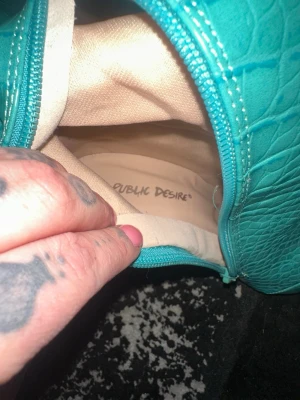 Turkosa stövlar från Public Desire - Säljer ett par höga turkosa stövlar från Public Desire med krokodilpräglat mönster. Skorna har spetsig tå, hög klack och dragkedja på insidan. Materialet är syntet med glansig finish och de går upp över knäet för en riktigt statement look.