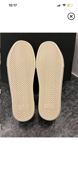 Svarta Saint Laurent sneakers - Säljer ett par svarta Saint Laurent sneakers med vit sula och handskriven logga på sidan. Skorna har snörning, rund tå och platt sula. Ovandelen är i textil och skinn, med klassisk Saint Laurent Paris-detalj på innersulan. Perfekt för dig som gillar stilrena och lyxiga sneakers.