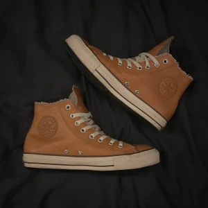 Bruna Converse sneakers i skinn - Säljer ett par bruna Converse high-top sneakers i skinn med vit sula och snörning. Insidan är fodrad med mjukt material för extra värme. Skorna är storlek 40 men passar även 41 skulle jag säga. Klassisk rund tå och metallöglor för snören. Perfekt för dig som vill ha en snygg och bekväm sko med lite extra edge.