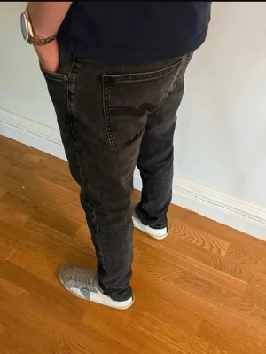 Svarta Nudie jeans - Säljer ett par Nudie jeans Lean Dean i svart tvätt med klassisk femficksdesign och smal passform. Jeansen har snygga detaljer på bakfickan och är tillverkade i stretchigt denim för extra komfort. Perfekta för dig som gillar stilrena och moderna jeans.