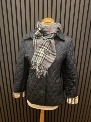   Scarf från Burberry - Quiltad grå scarf från Burberry med klassisk krage och snygga rutiga detaljer. Perfekt för dig som vill ha en stilren och tidlös look.