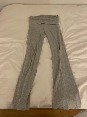 Grå bootcut mjukisbyxor - Säljer ett par grå mjukisbyxor med bootcut-ben och bred linning. Byxorna är gjorda i mjukt och stretchigt material, perfekta för chill dagar. Färgen är ljusgrå och tyget har en lätt melerad look. Passformen är loose och de har en skön, avslappnad vibe. Byxorna har 2 fläckar på låren på framsidan och de är lite slitna vid fötterna.