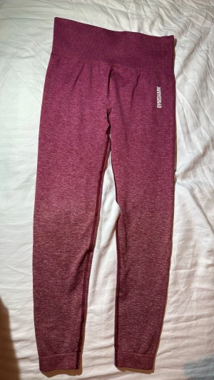 Vinröda seamless leggings från Gymshark - Supersnygga vinröda seamless leggings från Gymshark med hög midja och diskret logga på höften. Stretchigt material som sitter tight och formar sig efter kroppen. Perfekta för träning eller chill. Materialmix med polyester och elastan.