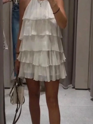 Vit volangklänning med halterneck - Säljer en söt vit kortklänning med flera lager volanger och halterneck. Klänningen är ärmlös och har en luftig, flowy passform som passar perfekt till sommaren. Perfekt för dig som gillar en romantisk och trendig stil.