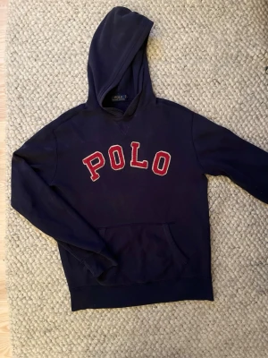 Marinblå hoodie från Polo Ralph Lauren🙌🤩 - Snygg marinblå hoodie från Polo Ralph Lauren med stor röd POLO-text på bröstet. Klassisk huva och känguruficka framtill. Tillverkad i mjukt bomullsmaterial som är perfekt för en avslappnad och sportig stil. I Stolek S🙌