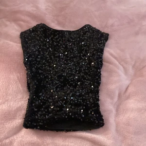 Svart paljettopp från Gina 💗💗 - Snygg svart topp täckt med glittriga paljetter. Modellen är croppad med rund hals och ärmlös design, perfekt för fest eller cool style. Tyget är mjukt och stretchigt för en bekväm passform. Perfekt för dig som vill ha något extra till outfiten! Har en öppen rygg som är skiiitsnyggt!!! 💗💗💗Säljer för att den tyvärr har blivit för liten.. 😢
