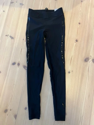 Svarta träningstights från Casall - Snygga svarta träningstights från Casall med glansiga detaljer längs sidorna. Deras sculpture modell. 