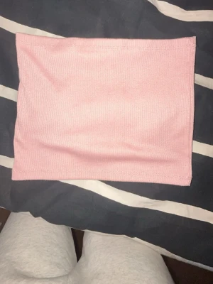 Ljusrosa ribbad tubtopp - Säljer en ljusrosa ribbad tubtopp som är perfekt för sommaren. Toppen är axelbandslös och har en enkel, stilren design som passar till många olika outfits. Materialet är mjukt och stretchigt för en bekväm passform.