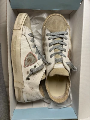Philippe Model vita sneakers storlek 40 - Säljer ett par Philippe Model sneakers i vitt skinn med grå snörning och beige mockadetaljer på tån och hälen. Sidan har den klassiska sköldloggan och yttersulan är i gummi med texten 'PHILIPPE MODEL'. Perfekta för en avslappnad streetstil.
