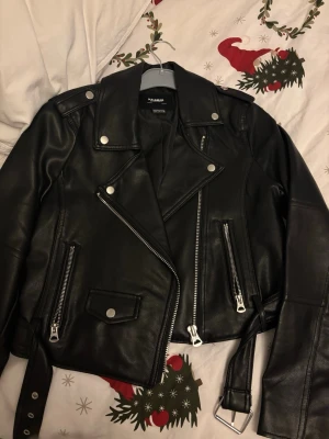 Svart skinnjacka från Pull&Bear - Snygg svart skinnjacka från Pull&Bear. Jackan har silvriga dragkedjor, axelklaffar, bälte i midjan och flera fickor. Väldigt fint skick då jag knappt använt den. 