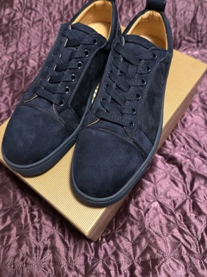 Christian Louboutin  - Stilrena svarta sneakers i mocka med rund tå och klassisk snörning. Skorna har en låg profil och diskret design som passar till det mesta. Insidan är fodrad i beige och sulan är svart för en enhetlig look. Oandvända