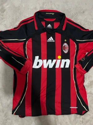 AC Milan långärmad matchtröja Adidas - Säljer en långärmad AC Milan matchtröja från Adidas med Kaka #22 på ryggen. Tröjan är röd och svart med gulddetaljer, klubbmärke och sponsortryck på bröstet. Tillverkad i funktionsmaterial, perfekt för fotboll eller samling.